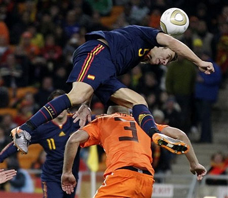 Spain's Carles Puyol, top, tries to score a goal as Netherlands' John Heitinga, bottom, goes to block him during the World Cup final soccer match between the Netherlands and Spain at Soccer City in Johannesburg, South Africa, Sunday, July 11, 2010